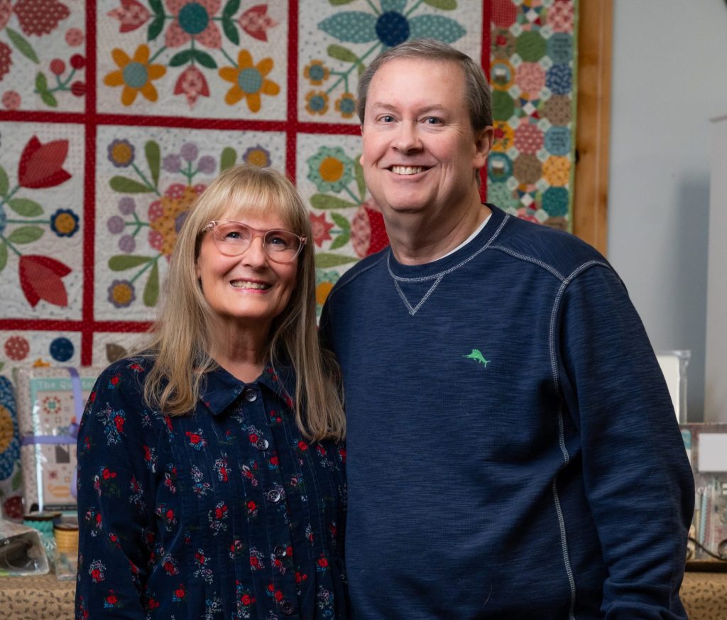 a woman and man standing in front of a handmade quilt