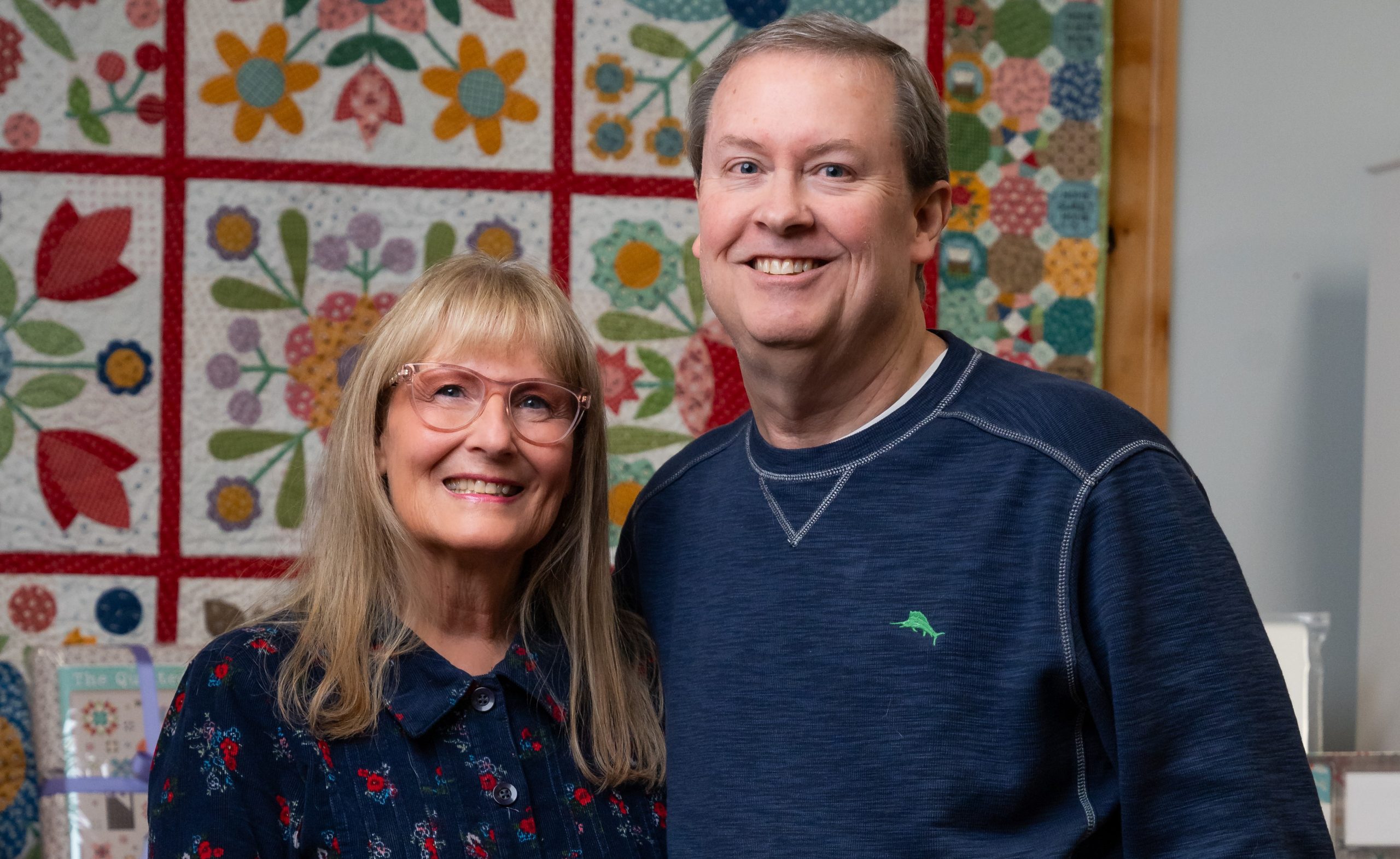 a couple stands in front of a handmade quilt