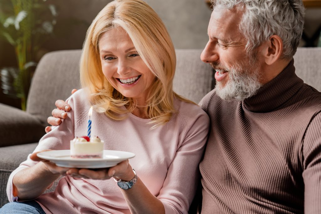 Happy senior couple celebrating anniversary or birthday with cake and candle