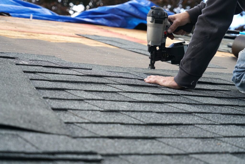 contractor using nail gun to install shingle to repair roof